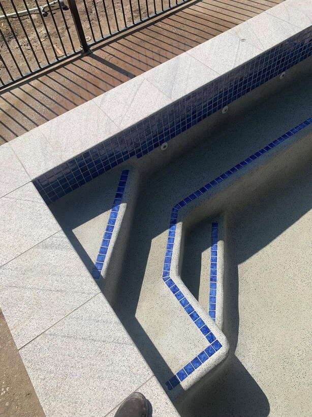 Empty pool corner with blue tile-edged steps and granite coping