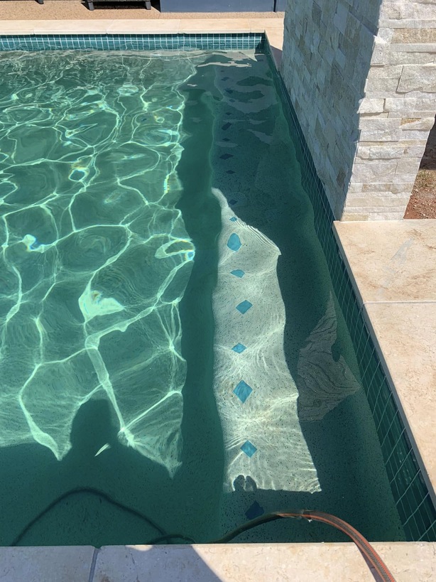 Clear pool with tile-marked steps beside a stone-clad wall
