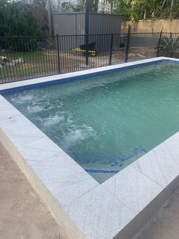 Rectangular pool with granite coping and jets running inside a black pool fence