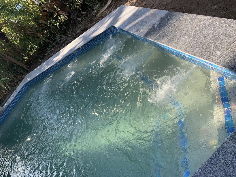 Pool corner with jets running, a blue tiled waterline and granite coping