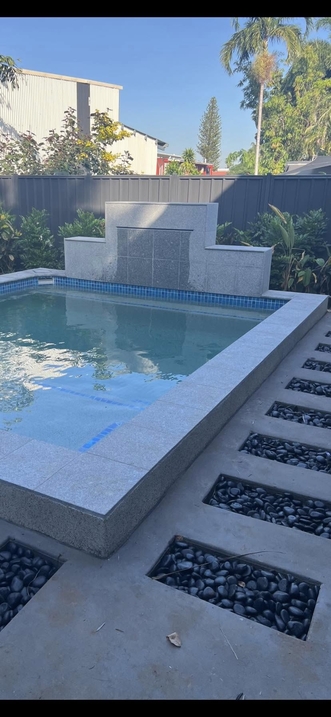 Pool with a water feature wall and stepping pavers set in black pebbles