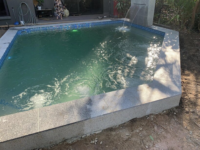 Raised pool with granite coping and a wall-mounted water spout