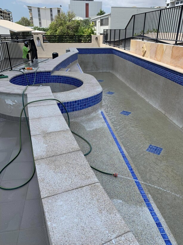 Long pool with a round spa nearly finished, blue tile lane line and hoses inside