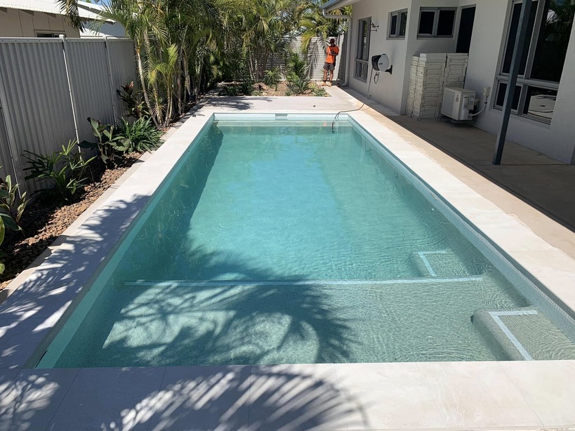 Long rectangular pool with pale coping between a fence and a house