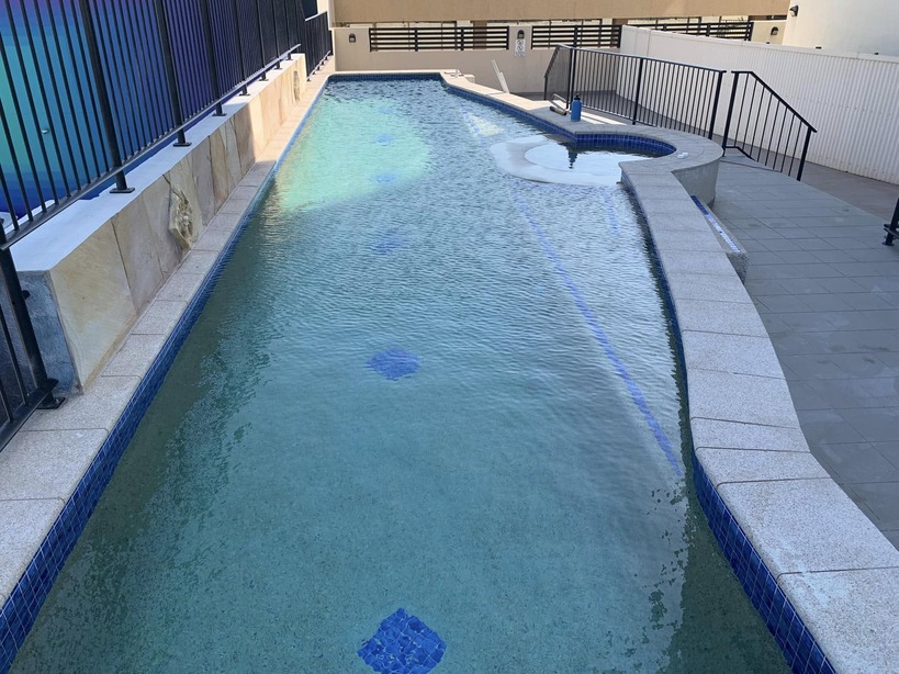 Long curved lap pool with a round spa at the end, beside a black fence