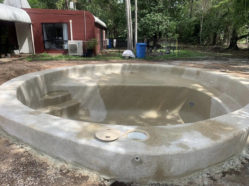 Round concrete spa shell under construction in a backyard