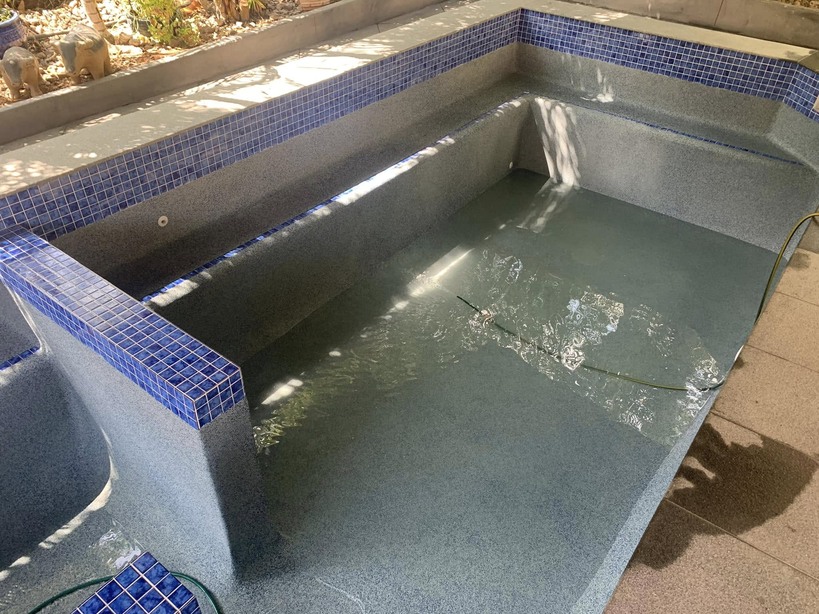 Pool filling with water, with blue mosaic tile edging and a raised spa wall