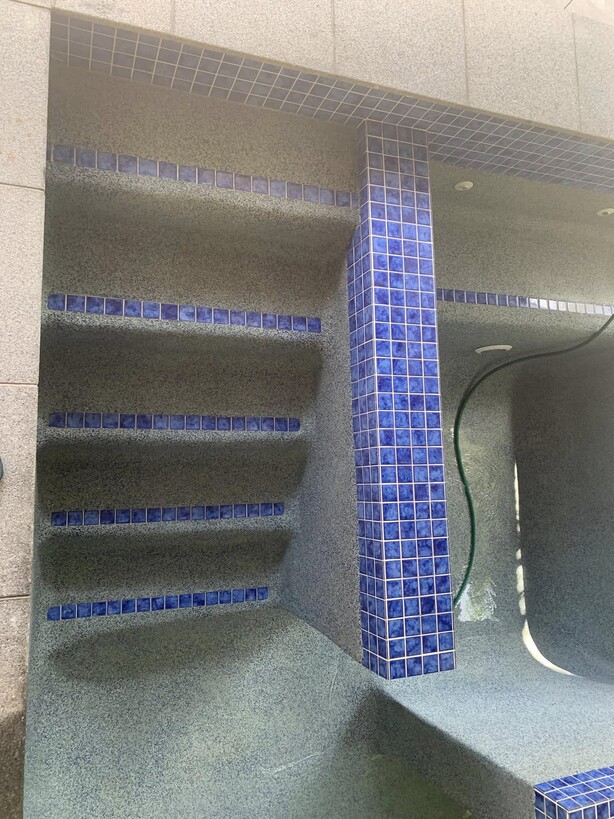 Empty pool with tile-edged steps and a blue mosaic tile column