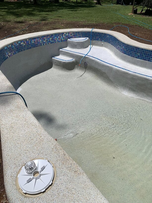 Freeform pool with curved steps and mosaic tile edging, partly filled