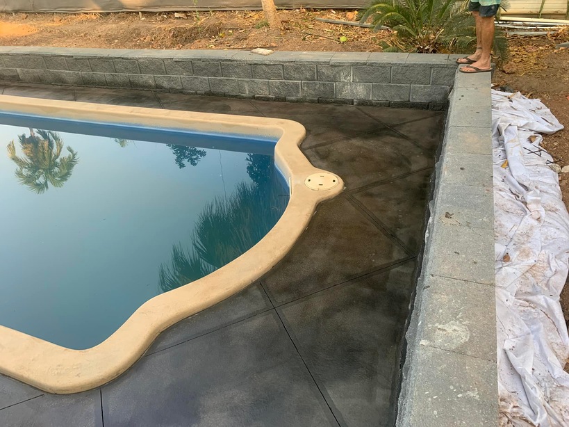Pool with cream coping and a dark concrete surround beside a block wall