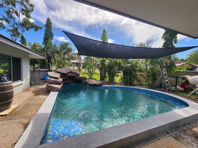 Curved pool with a rock feature under a shade sail beside a house