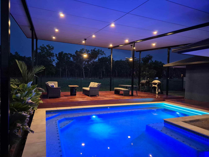 Pool lit blue at night beside a covered timber deck with outdoor lounge furniture