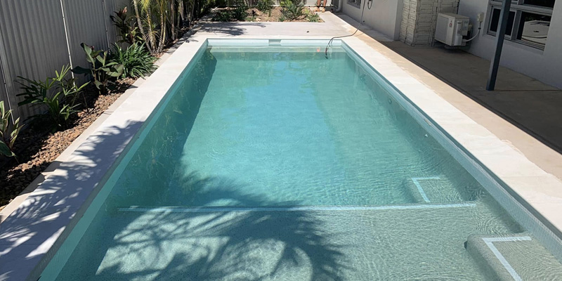 Long rectangular pool with pale coping beside a house and tropical garden