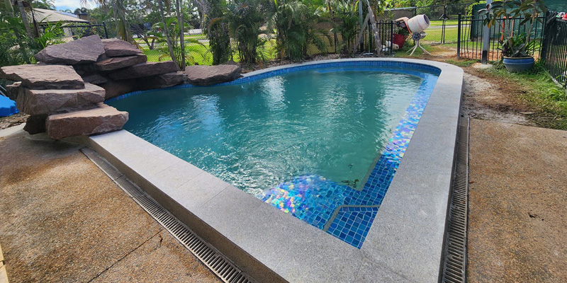 Curved pool with a rock feature, blue mosaic step tiles and granite coping