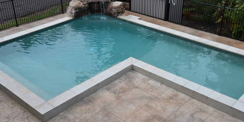 L-shaped pool with a rock waterfall and patterned paving around it